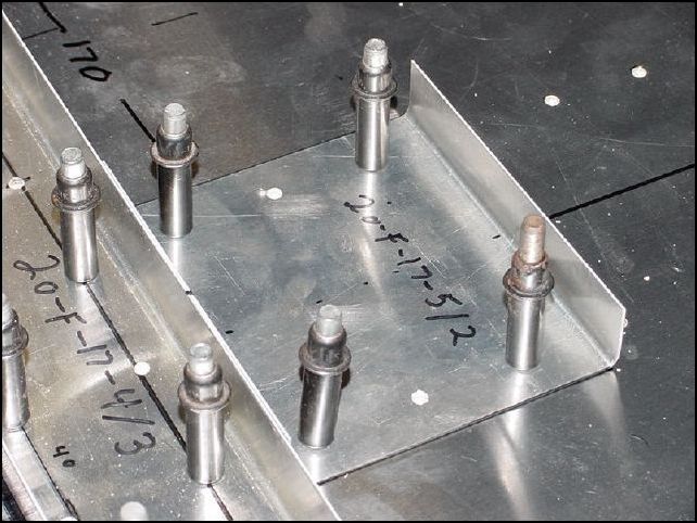 Position the center bearing channel to the floor skin.  This channel is lined up with the center line of the floor and AGAINST the forward floor channel.  Drill the 6 A5 holes and cleco in place.  NOTE:  These holes are already drilled in the floor skin so be sure to drill them from the other side.  I did this by clamping the bearing channel to the floor channel then pulling the assembly forward over the edge of the table and drilling from underneath.  It helps to have a friend to help you with this step.