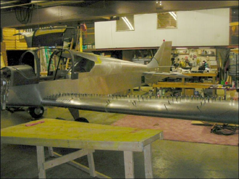 Deburr, clean, prime, and rivet the flap to the wing.  Deburr, clean, and prime all top skins.  Trim inboard skin to fit the shape of the fuselage.  Drill holes in side of fuselage for wires, pitot, static, and control cables.  Bolt wing to aircraft!